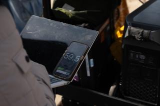 Crew member checking a reading on a phone balanced against a laptop beside the battery station on the cart