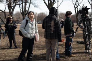 Crew waiting between setups on the grass, camera on sticks and the boom raised at the edge of frame
