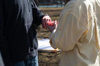 Two hands meeting over a folded pink paper flower being passed between the actors