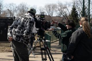 The slate held up in front of the lens while the operator and the script supervisor watch the frame