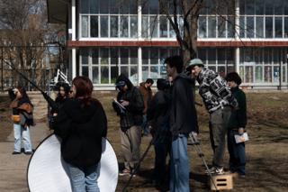 A crew member carrying the round reflector across to the camera, the schoolyard fence behind