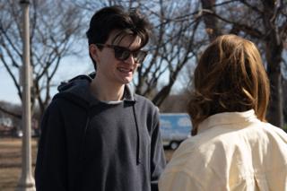 The actor in sunglasses laughing mid-sentence as the actress listens, bare trees behind them