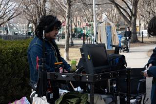 Crew member in headphones working at the monitor cart, the park playground behind him
