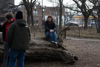 A crew member sitting out on the fallen log while two of the company talk in the foreground