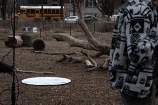 A silver reflector laid flat on the ground among the cut logs, the street and a school bus beyond