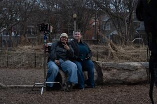 Two of the crew perched on the log beside the camera, grinning at the lens