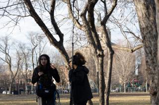 The sound recordist and boom operator crossing under the bare trees, mixer bag and cable slung at her side