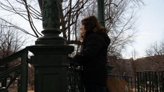 A figure leaning on the bandstand railing looking out across the park, backlit by the low sun