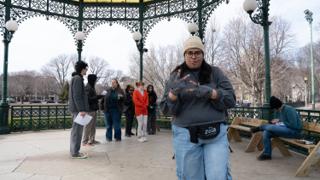 The assistant director calling the next move with both hands raised, marks taped on the bandstand floor behind