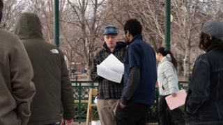 The director reading through the pages in the middle of the company, a pink folder held at the edge of frame