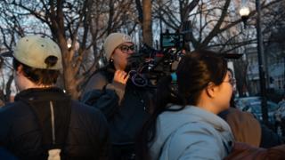 The operator with the rig on his shoulder at dusk, the monitor lit against the bare trees