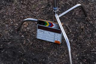 Close on the clapperboard propped against the tripod legs on the ground, marked If I Could Touch the Sun, scene 8A take 1