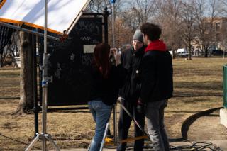 Three of the crew rigging a light stand in front of the chalkboard, the silk frame overhead
