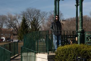 The actor in sunglasses and a grey coat standing at the bandstand railing