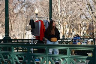 A crew member at the wardrobe rack behind the green ironwork railings, coats and shirts hung out in the sun