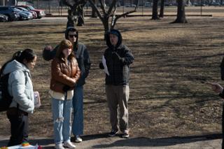 Four of the company standing on the open ground with a script, one gesturing off toward the setup