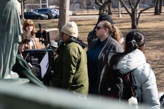The crew crowded in around the camera and monitor beside the statue, the actor waiting in the sun beyond