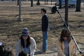 The actor alone on the path mid-take, the boom microphone reaching in over two of the cast in the foreground