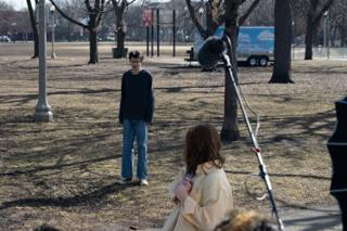 The actor standing off across the lawn from the actress, the boom angled in and an ice cream truck parked beyond the trees