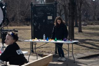 A crew member laying the folded cranes out in a line along the table in front of the chalkboard
