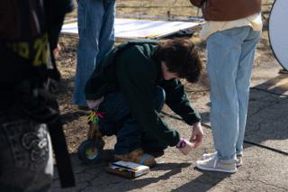 A crew member crouching to set the colour chart down on the path, cable and tape at his feet