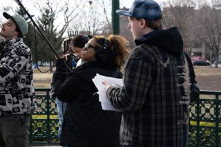 Boom raised overhead at the edge of frame while the script supervisor follows along on the sides