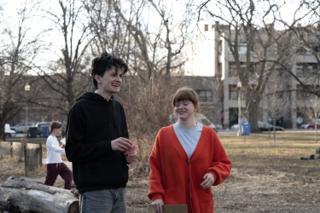 The two leads walking back laughing, the pink paper flower in his hand and the sign under her arm
