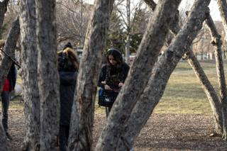 The sound recordist checking her mixer between the trunks, headphones on and the boom operator behind