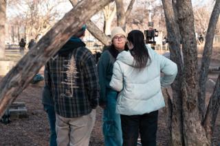 Three of the crew talking among the trees with the camera rig standing behind them