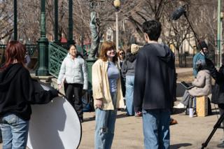 A reflector angled in on the two leads mid-scene, the boom overhead and the statue behind the bandstand railings