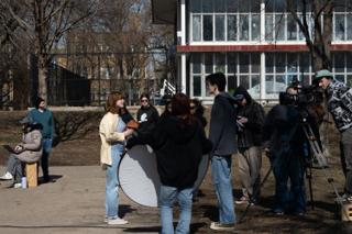 The actress lit with a round reflector held in close, the crew and camera gathered round and the school fence behind