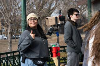 Crew member in a knit beanie grinning and giving a thumbs-up beside the built-up camera rig