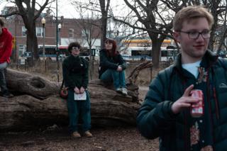 The cast sitting out the turnaround on the log, a crew member with a drink in the foreground