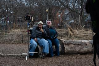 The same two laughing together on the log, the camera stood up on sticks beside them