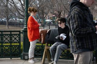 Actor on the bench laughing over his sides while a colleague in a red sweater stands talking with him