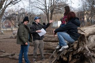 Director gesturing through the blocking to the cast gathered on the fallen log