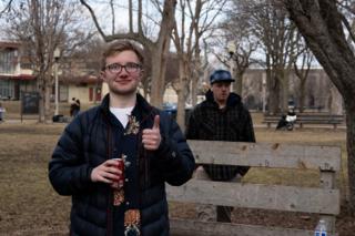 Crew member raising a thumbs-up to the camera, drink in hand, at the end of the day