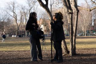 The two sound crew comparing notes under a tree, boom pole stood upright between them