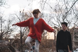 Actress in a red cardigan balancing along the fallen log with her arms out, the actor walking alongside