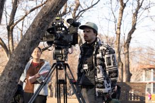 Operator at the camera on sticks with the script supervisor beside him, pages in hand
