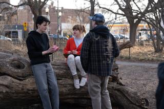 The director talking the beat through with both leads at the log, a paper flower in the actor's hand