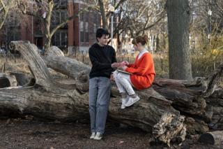 The actor offering the paper flower to the actress seated on the fallen log, mid-scene