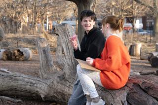 The two leads laughing together on the log between takes, the flower and the sign still in their hands