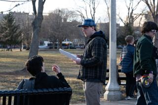 The director reading a line off the page to the actor on the bench, the unit moving behind them