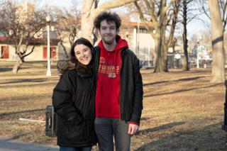Two of the company arm in arm at the edge of the park, grinning for the camera between setups