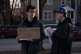 Crew member running the scene with the actor, script pages in hand, the hand-lettered sign held between them