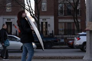 Crew member carrying a folded silver reflector along the sidewalk toward the corner