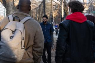 The actor walking the path toward camera, framed between two crew watching from the foreground