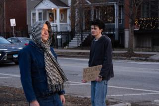 Two actors at the crossing, the sign held low as the scene resets