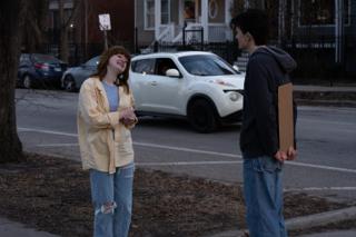 The two leads laughing between takes on the corner, the sign turned blank side out
